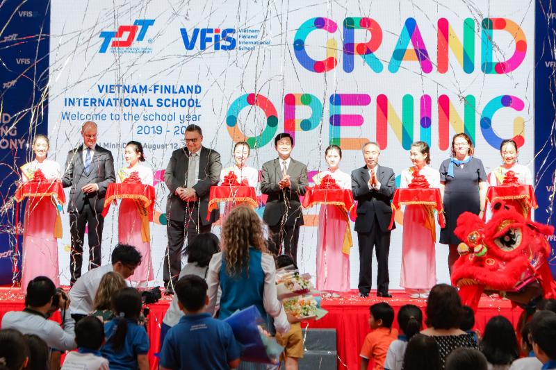 Finnish and Vietnamese official standing on a stage, ready to cut a ceremonial cord held by women dressed in traditional Vietnamese costume.